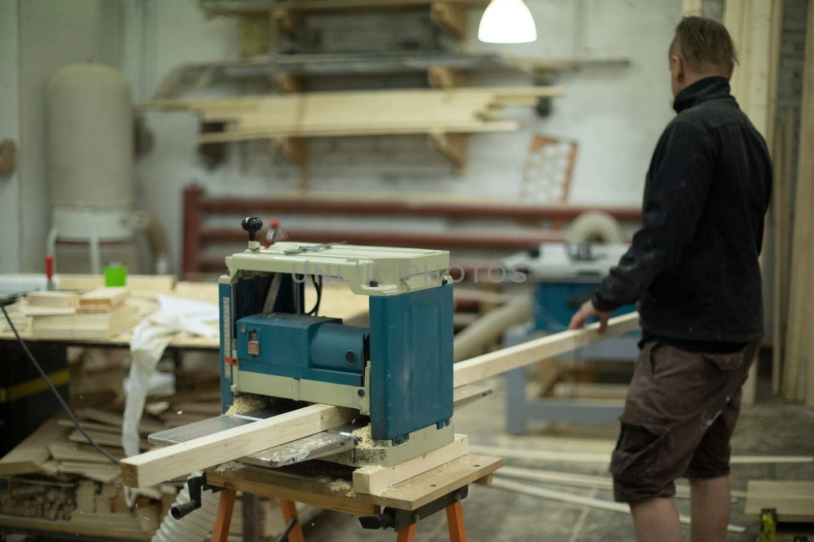 Guy is chipping board on machine. Worker makes furniture. Work in carpentry workshop.