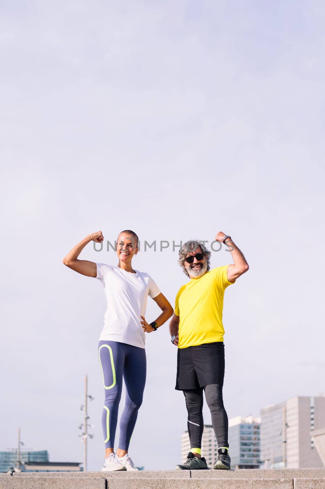 senior man and his personal trainer posing flexing muscle and smiling happy looking at camera, concept of active and healthy lifestyle in middle age, copy space for text