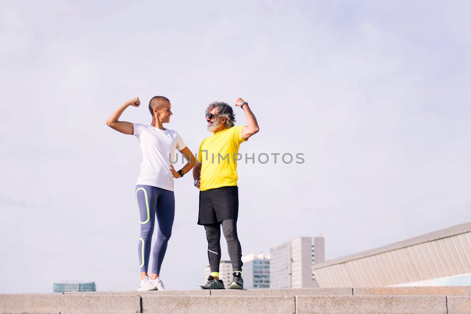 senior man and personal trainer celebrating success of the effort by showing muscle and smiling happy, concept of active and healthy lifestyle in middle age, copy space for text