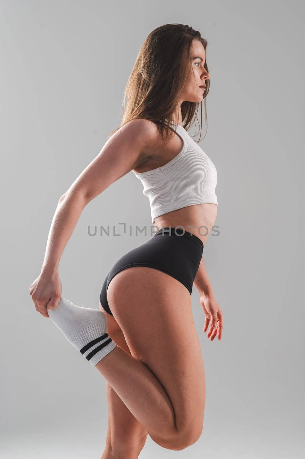 Athletic Caucasian woman stretching her quadriceps on a white background. Vertical photo. by mrwed54