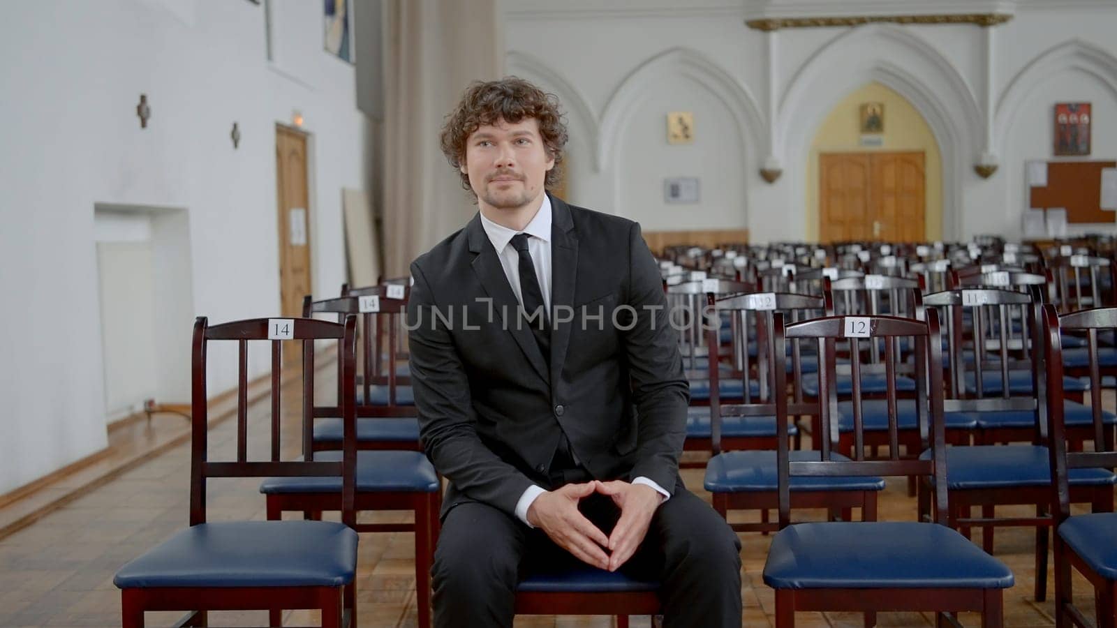 Groom in empty church. Action. Attractive man in suit is sitting alone in church. Groom is sitting alone and waiting for preparation of wedding ceremony. Rehearsal of wedding ceremony in temple.