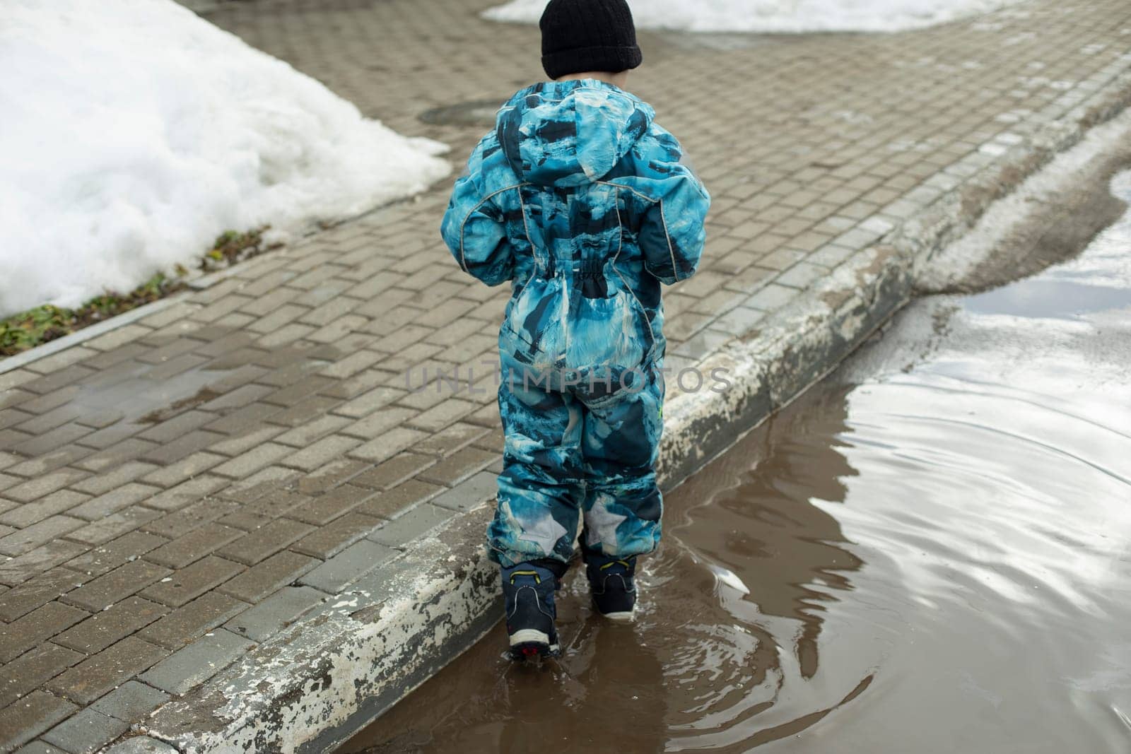Child in puddle. Preschooler in boots walks on water. Spring puddle.