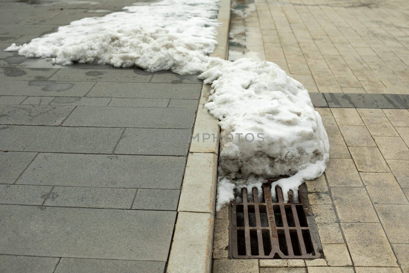 Snow melts at sewer grate. Removal of melt water from street. Sewer grate in city.