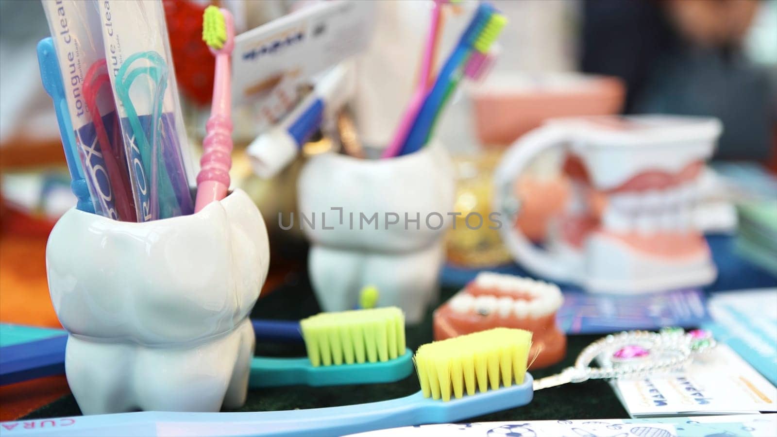 A large model of human jaw with white teeth, colorful toothbrushes, and a toy lying on the table, children dental clinics concept. Art. Close up for the dental instruments. by Mediawhalestock