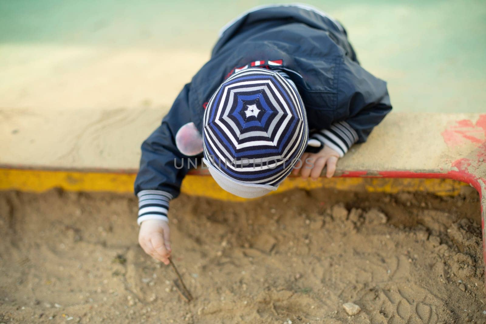 Child in sandbox. Preschooler on playground. Little boy digs ground.