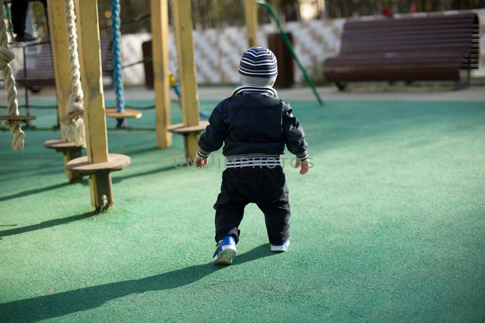 Baby on street. Child on playground. Little boy walks by himself. Child from behind.