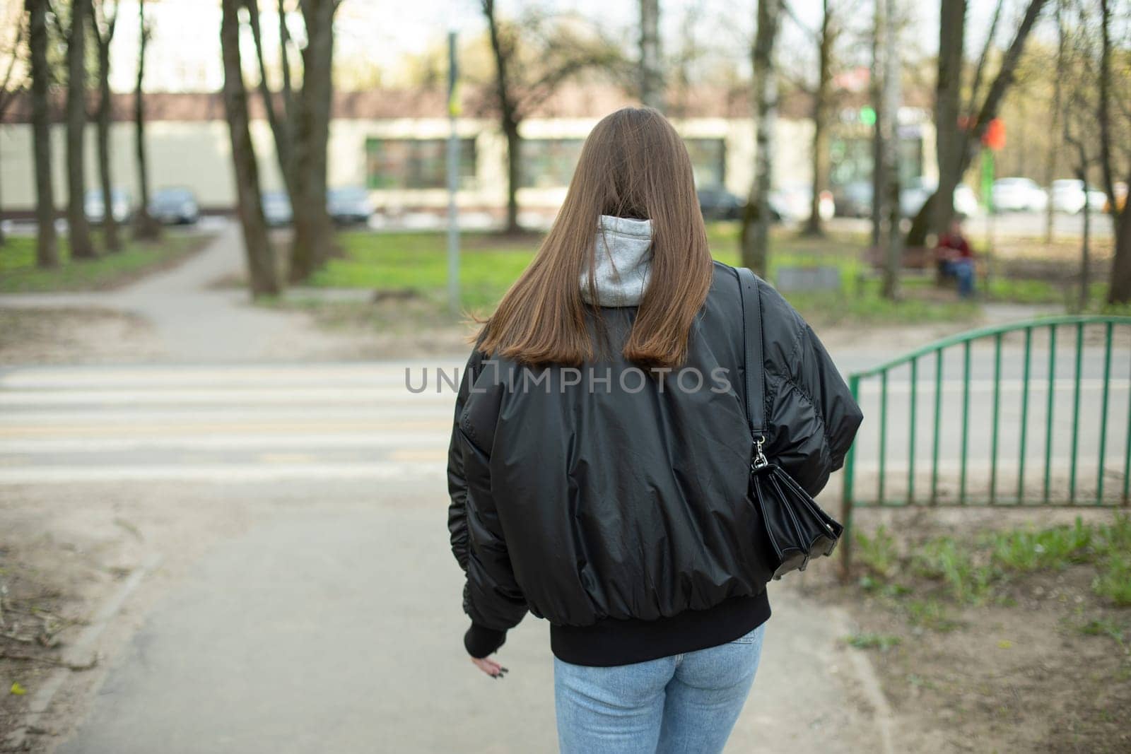 Girl in black jacket and blue jeans walks down street. Woman walks through city. Student on walk.