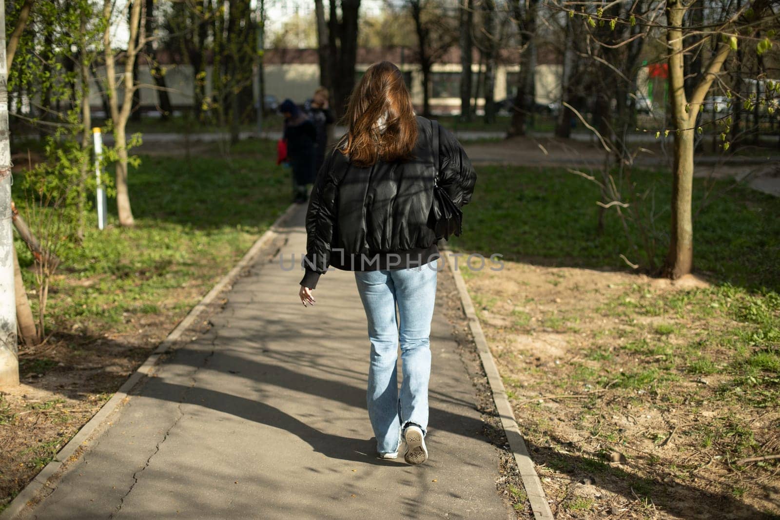 Girl in black jacket and blue jeans walks down street. Woman walks through city. Student on walk.