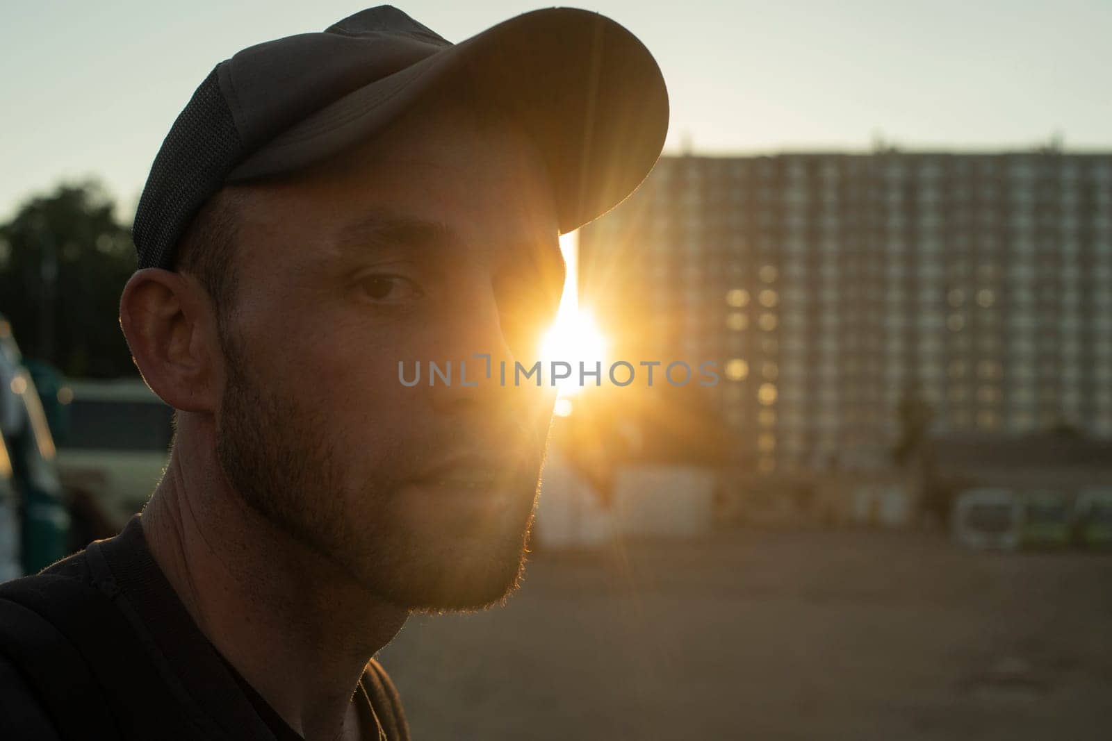 Portrait of guy in sun in city. Man at sunset. Rays of sun on his face. by OlegKopyov