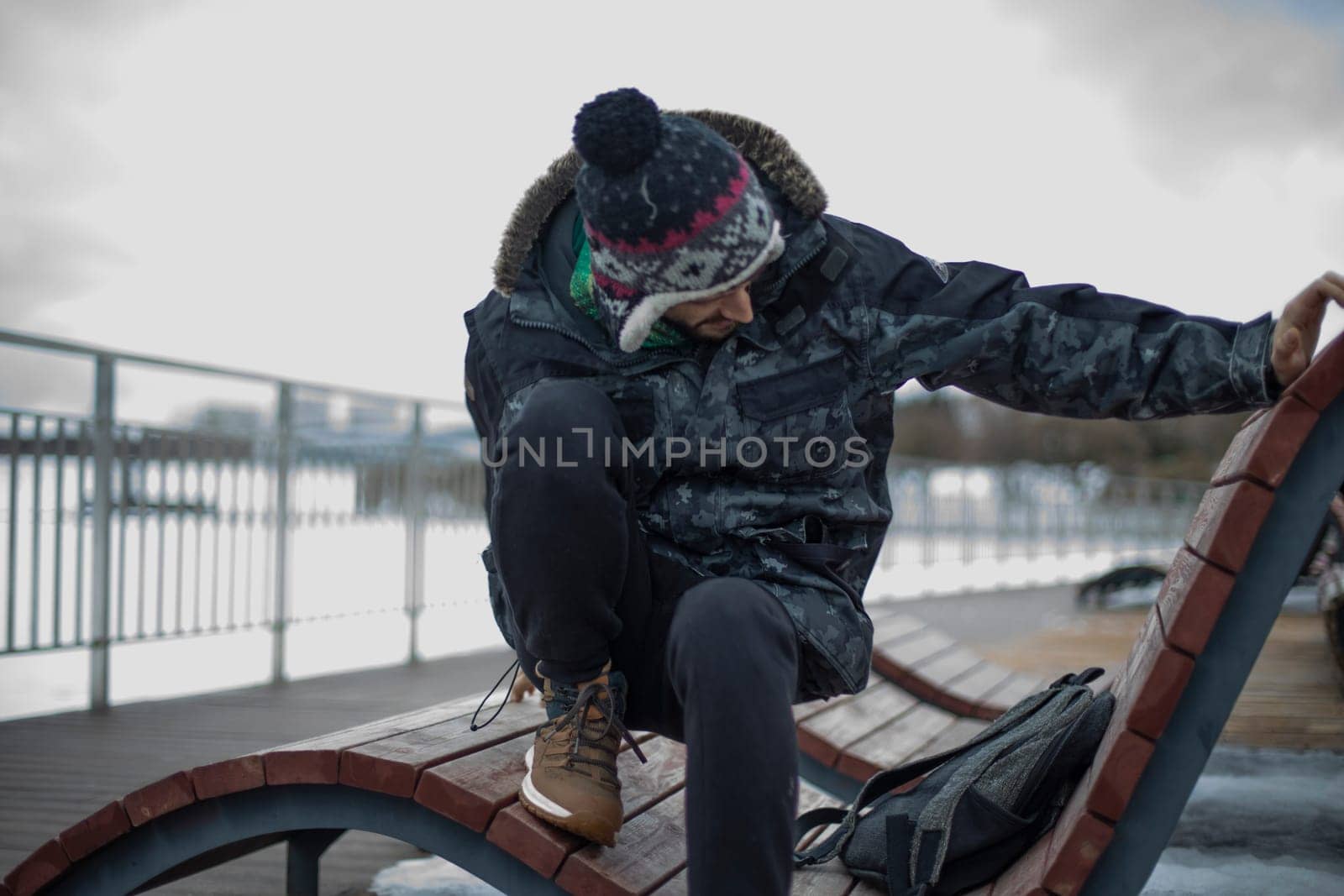 Guy on bench. Student gets up. Man in modern winter clothes. Man in park.