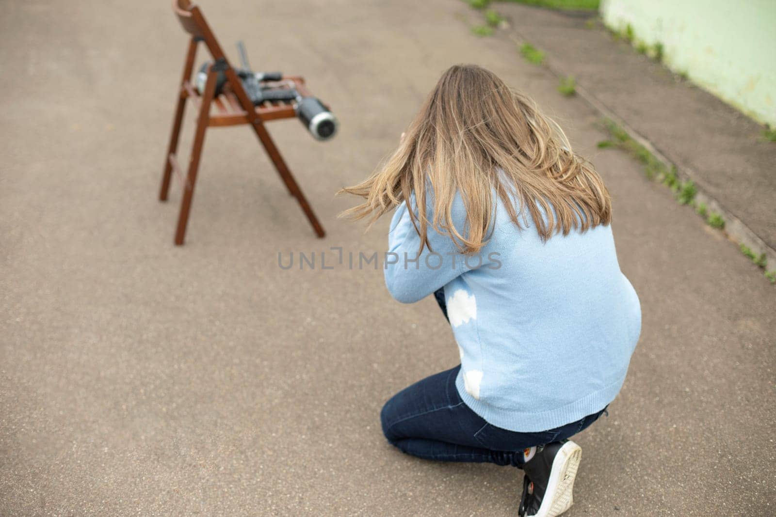 Girl is preparing to shoot. Shooting apprentice. Woman sits on pavement.