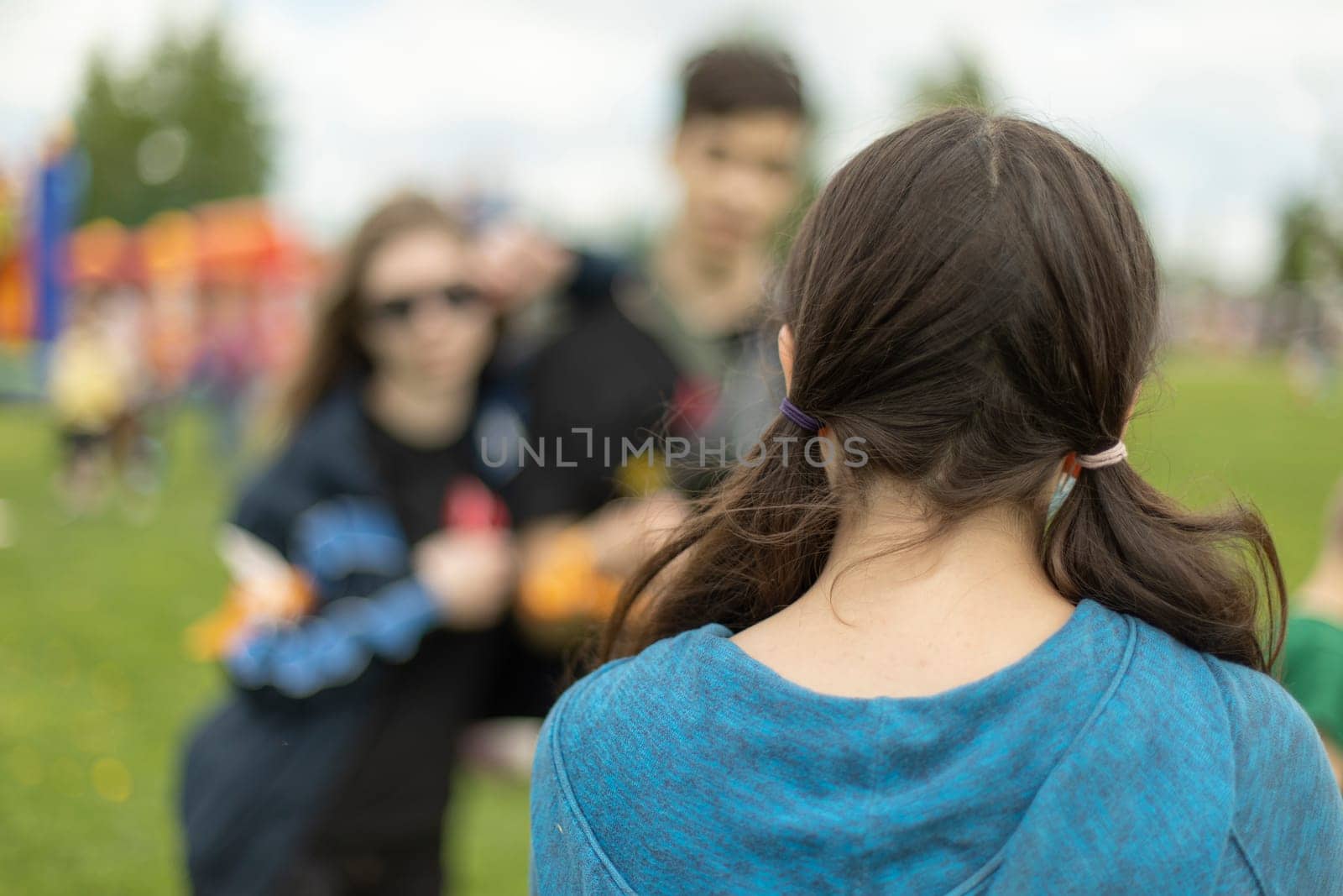 Teenagers in summer. Schoolgirl look at couple of friends. Girl from her back with her hair unpainted. Rest in summer in park.