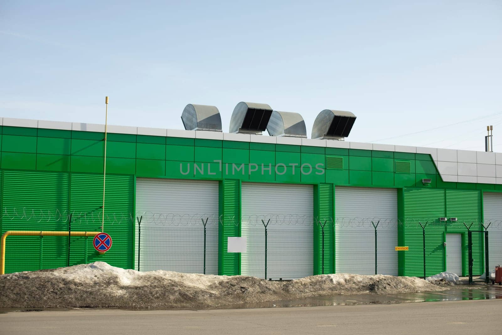 Green technical building. Garage for namesakes. Pipes on roof. Gate in house. Building is windowless.