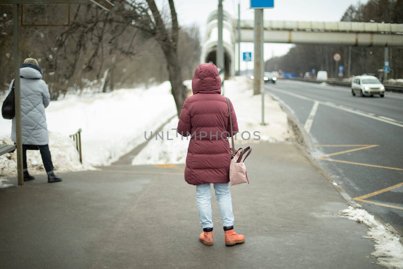 Girl is waiting for transport on road in winter. Girl is waiting for bus. by OlegKopyov