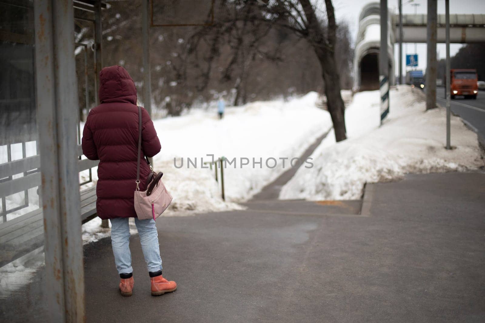 Bus stop in winter. Girl is waiting for bus. Transport on highway. by OlegKopyov