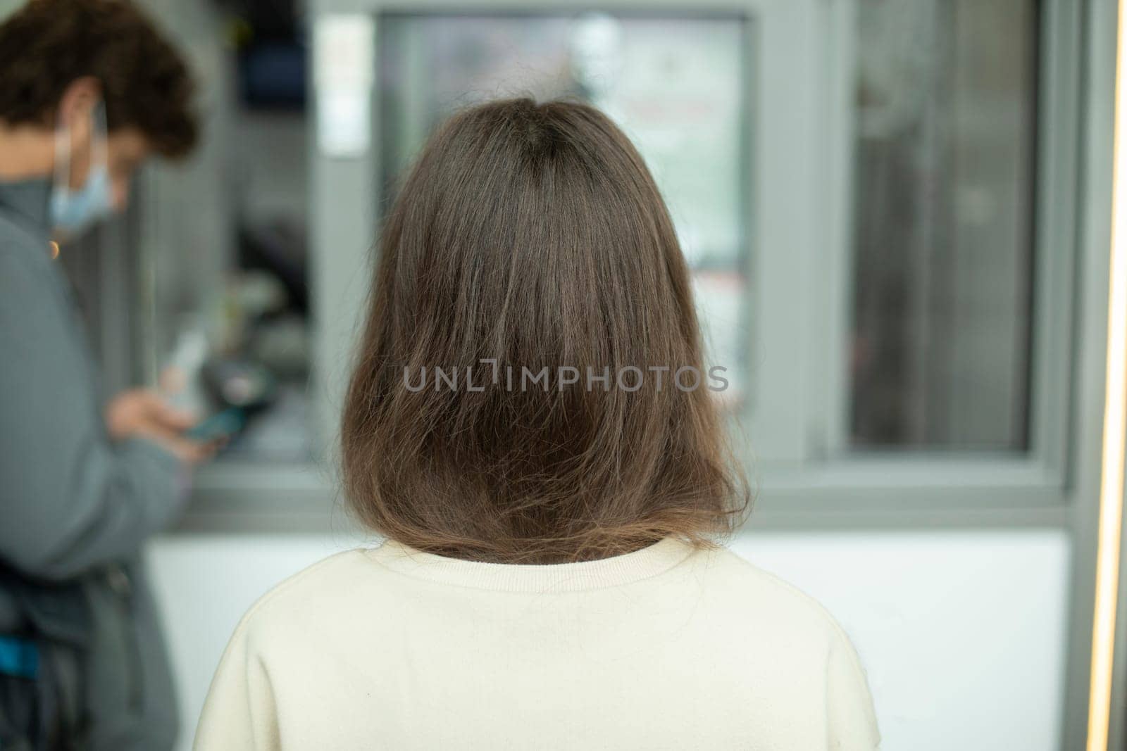 Girls hair from back. Girl in line. Brunette on street. White sweater. Uncolored hair on head.