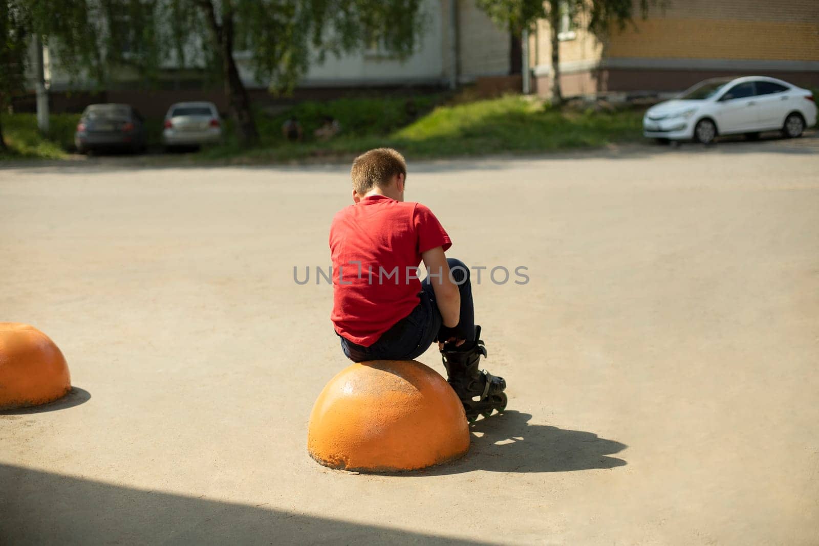 Child wears roller skates. Mask in red T-shirt. Schoolboy alone. Preparation for arrival. Roller skates in summer.