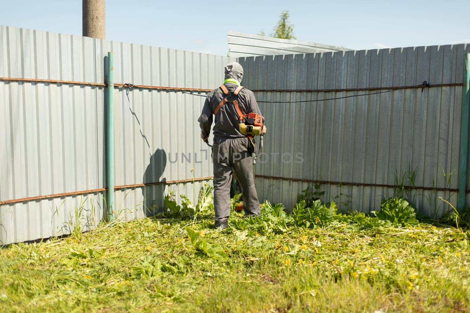 Man mows grass near fence. Man cuts lawn. Guy works as lawn mower.