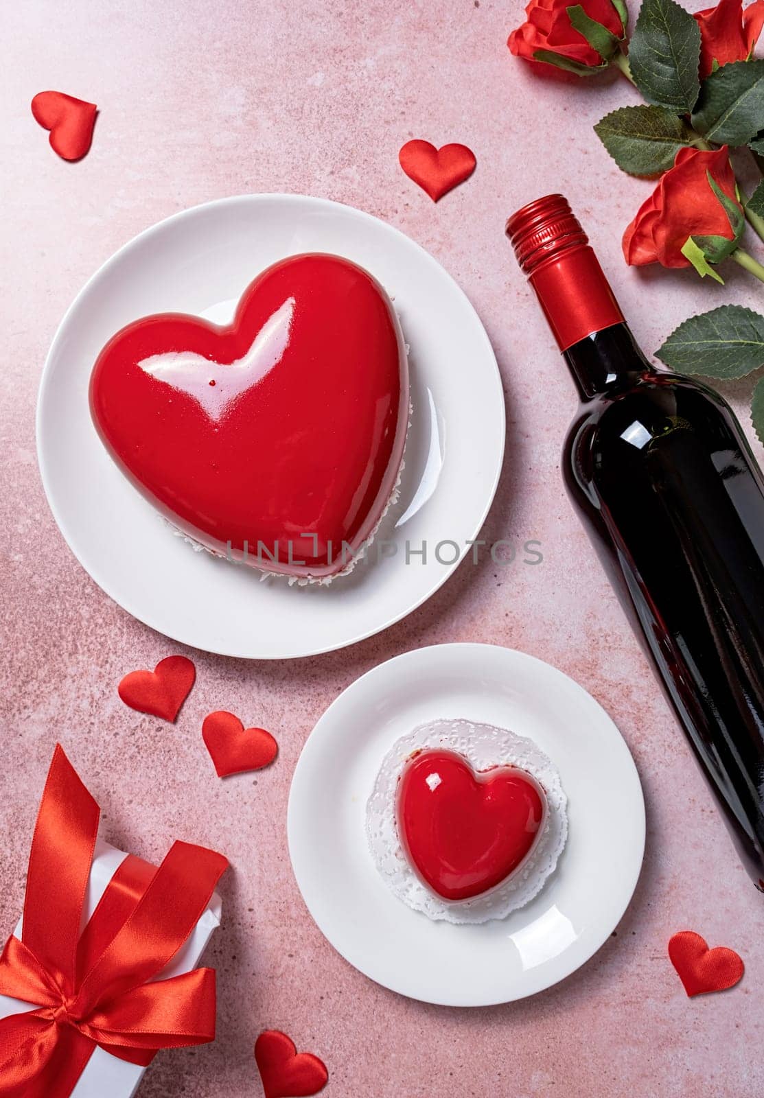 Valentines day. heart shaped glazed valentine cake, gift and wine on pink concrete background