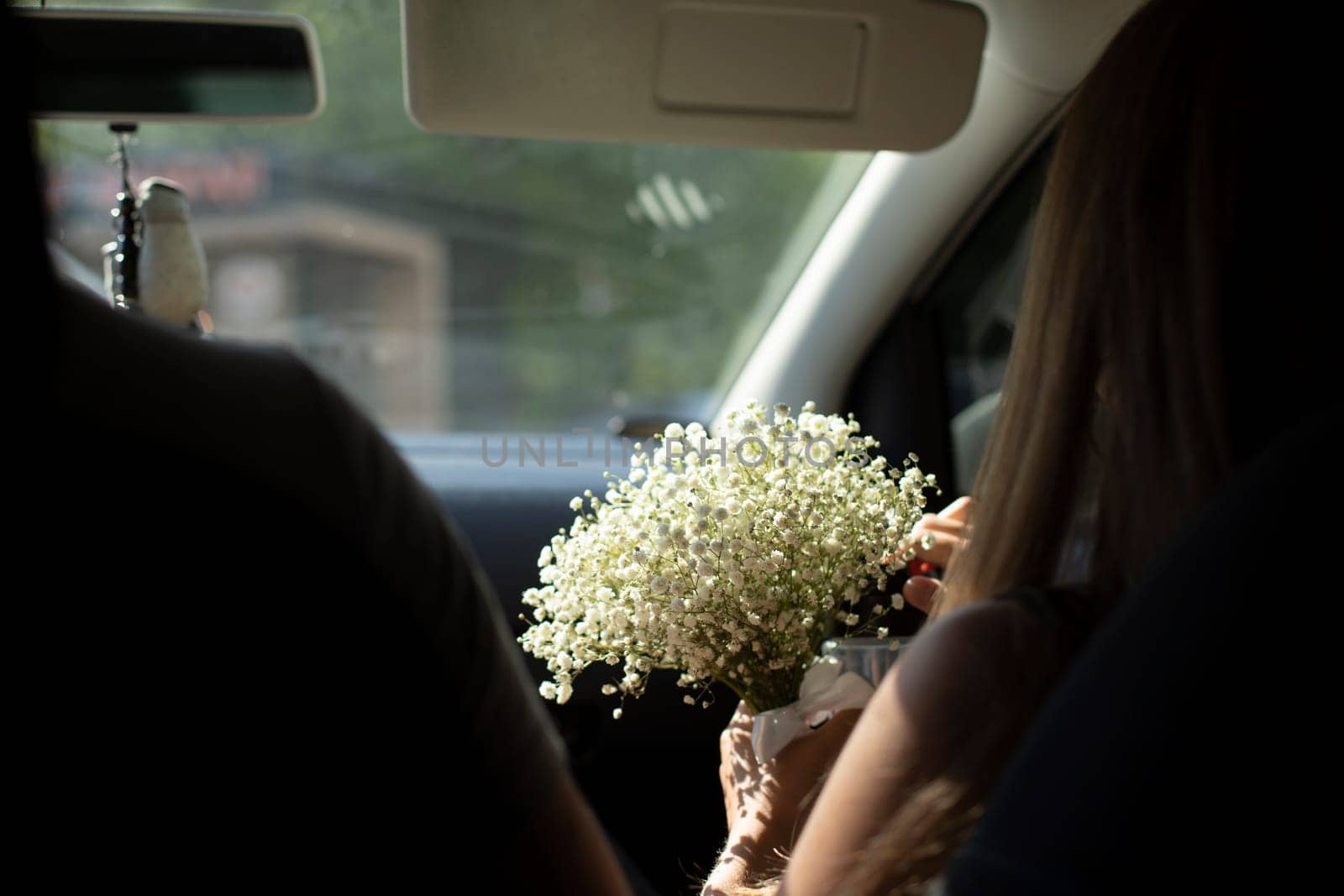 Bouquet of flowers in car. Bride's bouquet is in hands of girl. White flowers in hand. Gift to girl.