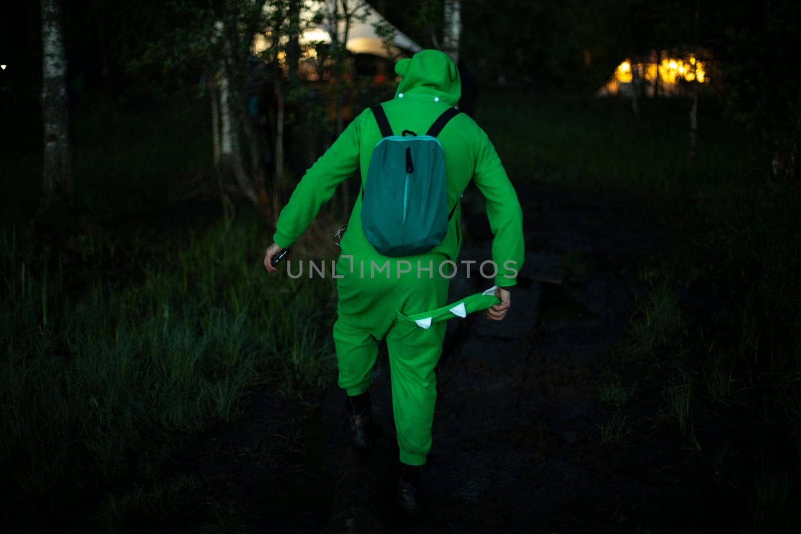 Man in green suit walks through woods. Guy in fun crocodile costume. by OlegKopyov