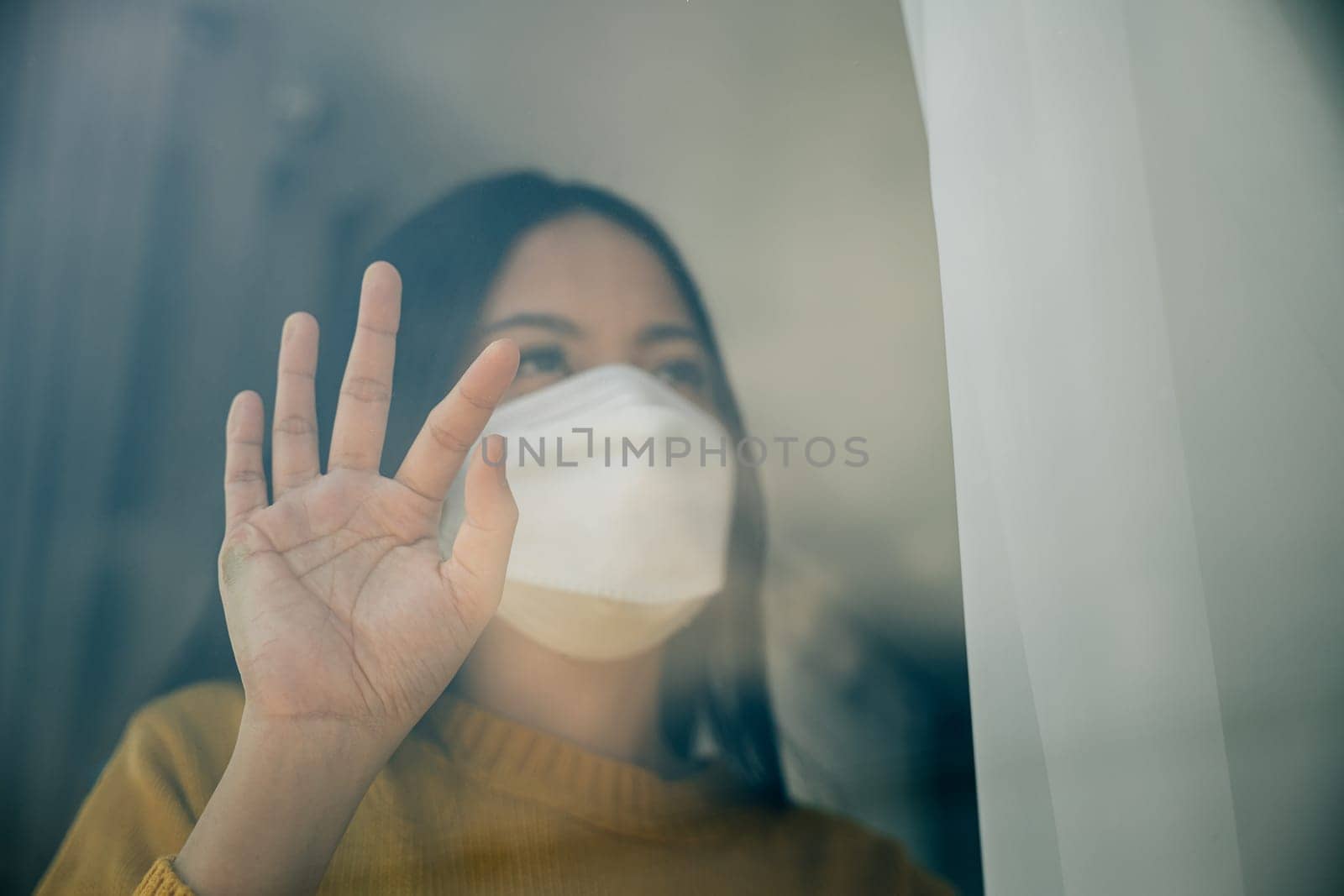 A woman wearing a medical mask practices self-isolation at home emphasizing COVID-19 prevention during the outbreak and the concept of home quarantine.