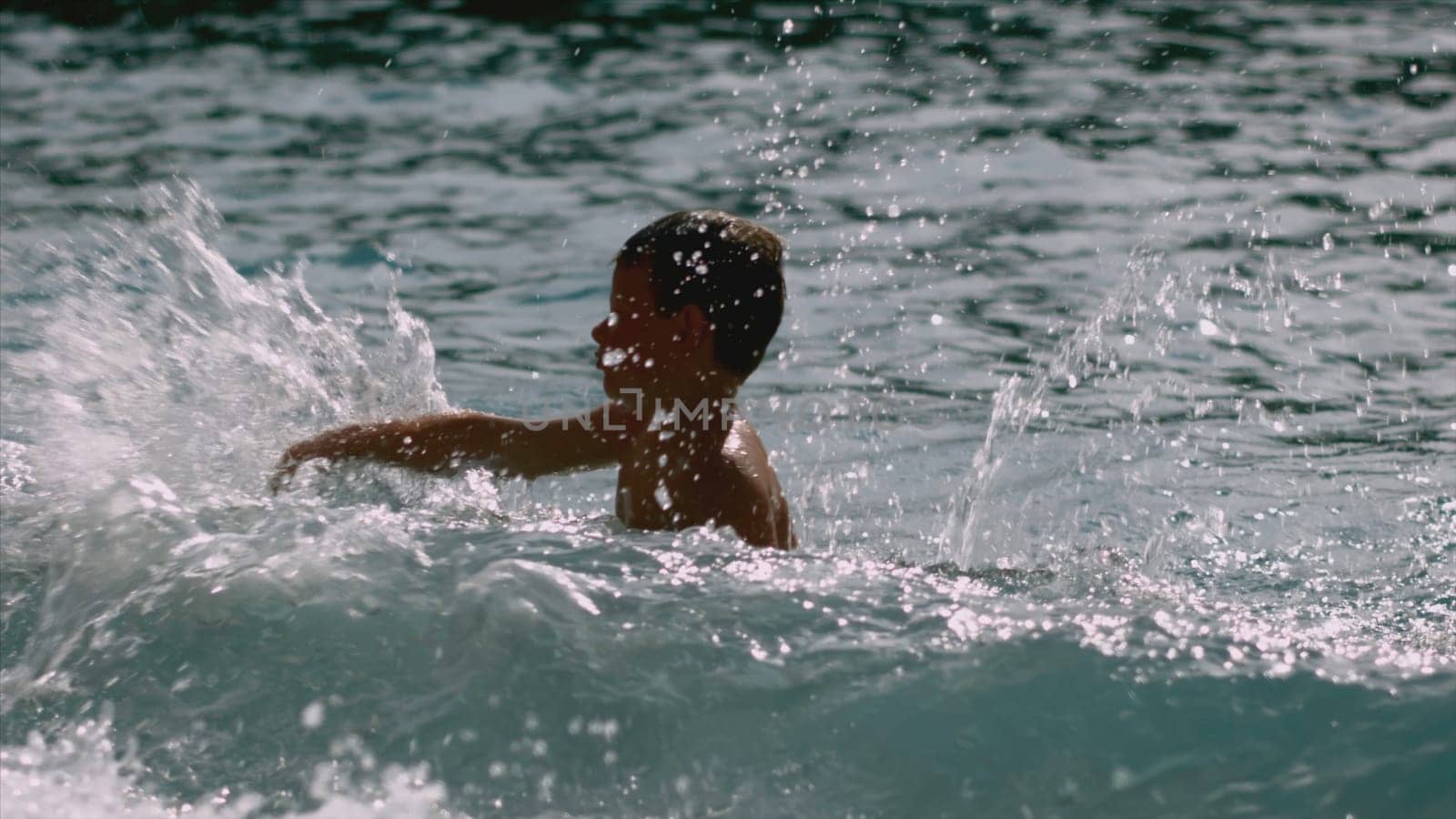 Boy swims in sea with waves. Creative. Boy swims alone on sea in sunny weather. Boy is resting on sea and swimming with waves and splashes.