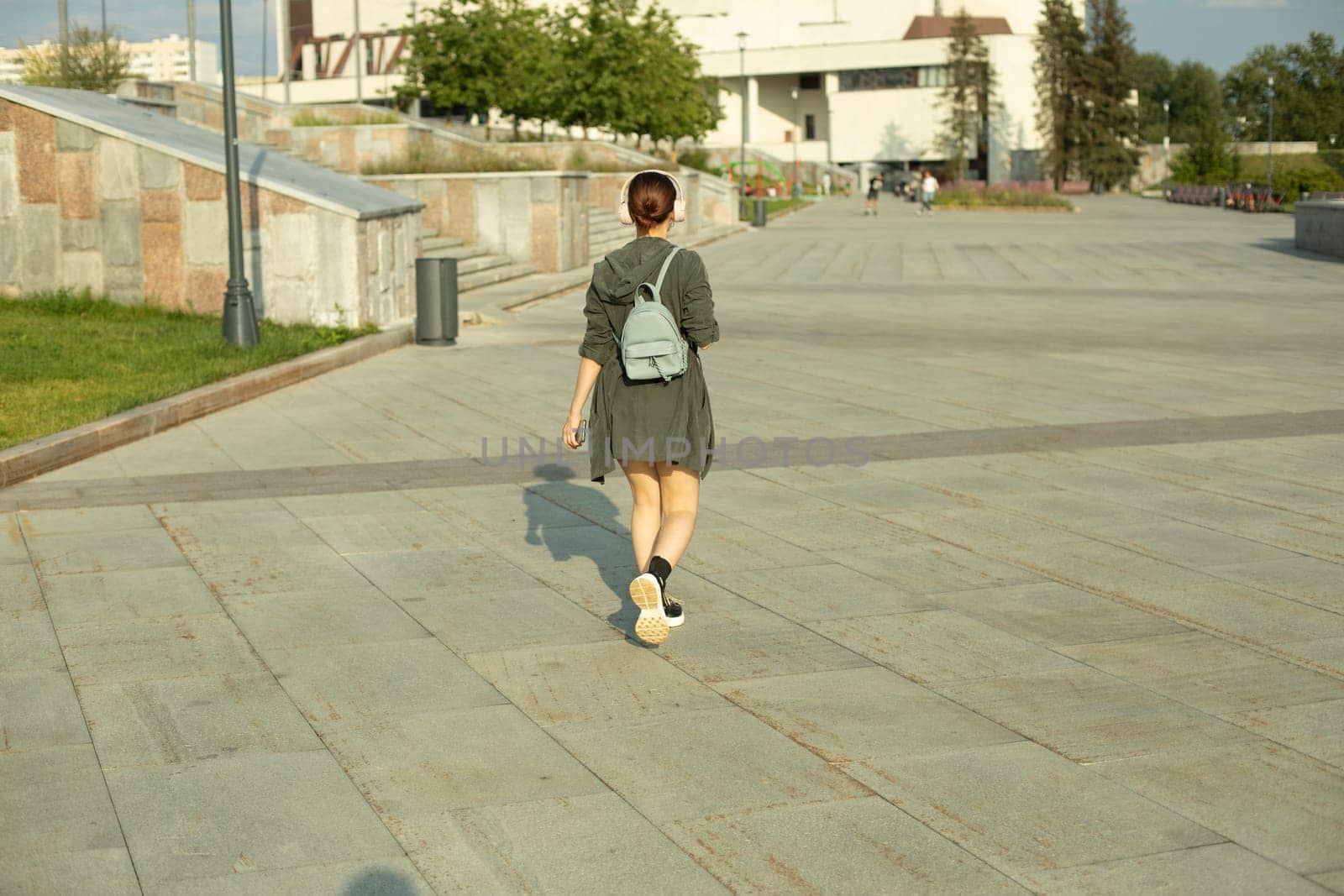 Girl walks through square in summer. Walk around city. Girl with small backpack. City is in summer.