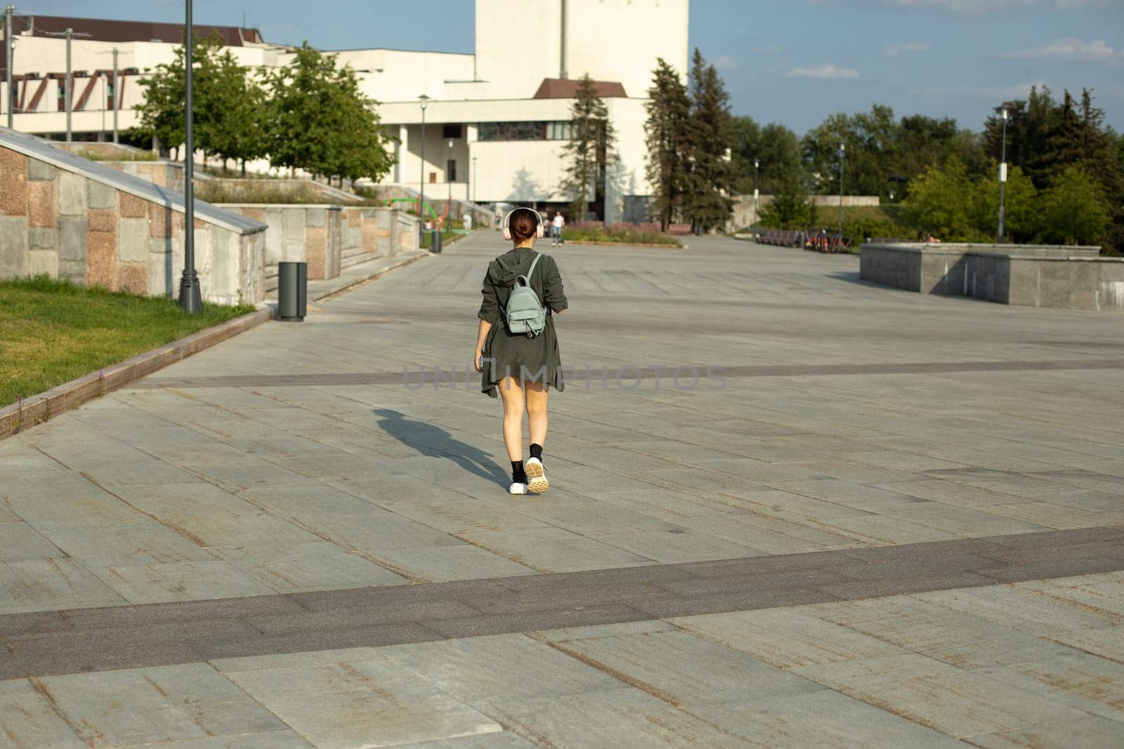 Girl walks through square in summer. Walk around city. Girl with small backpack. City is in summer.