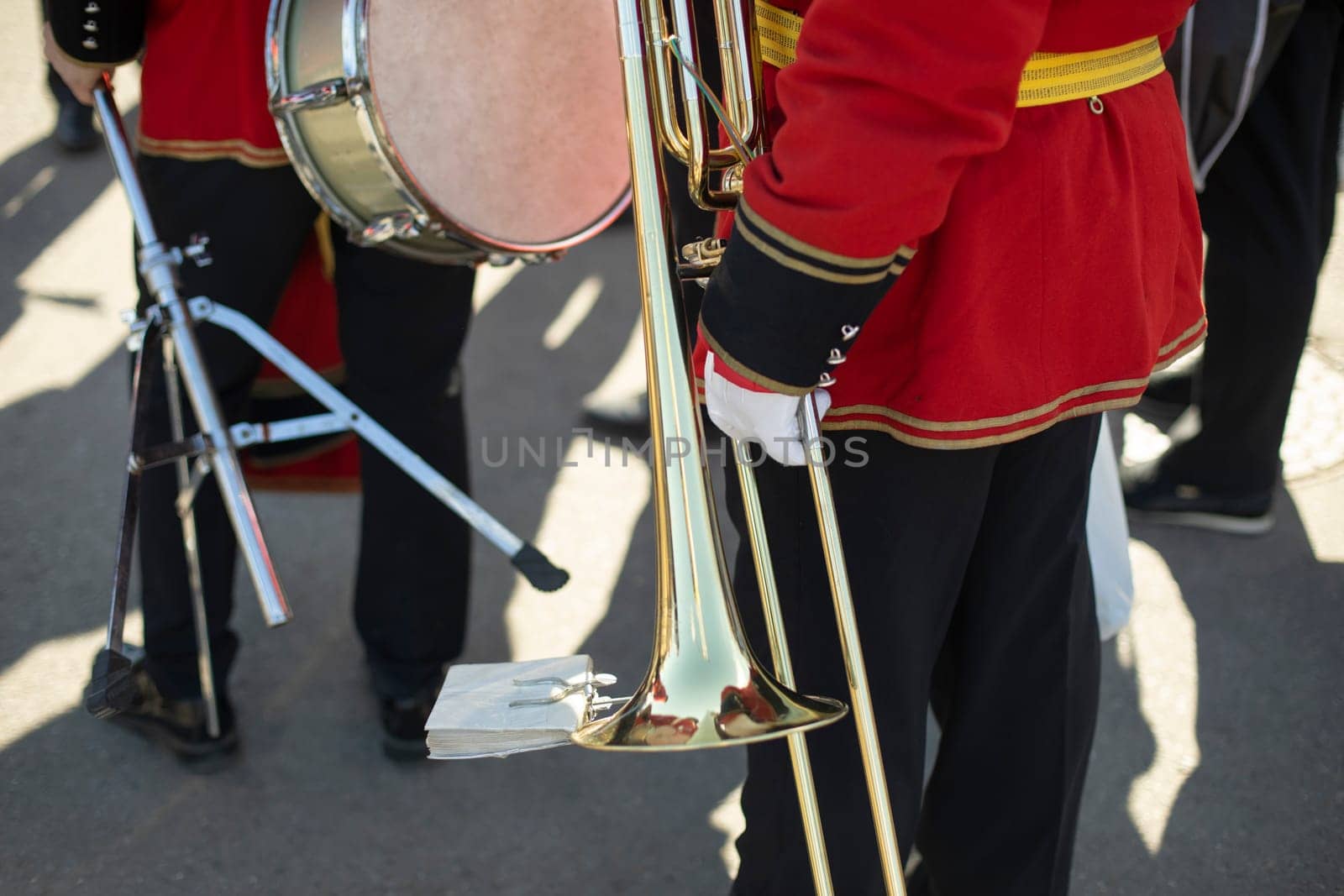 Orchestra member holds brass pipe. Trumpeter details. Ceremonial red uniform. Military band on street.