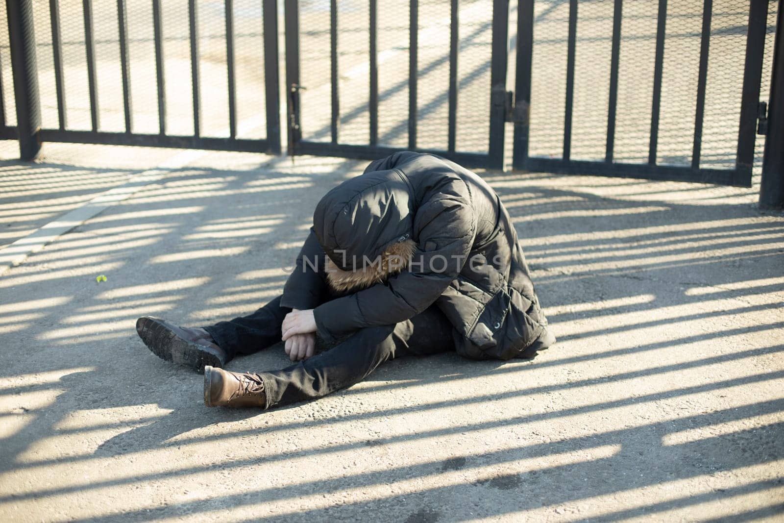 Guy is sitting on pavement. Homeless man on street. Drunk went downstairs. by OlegKopyov