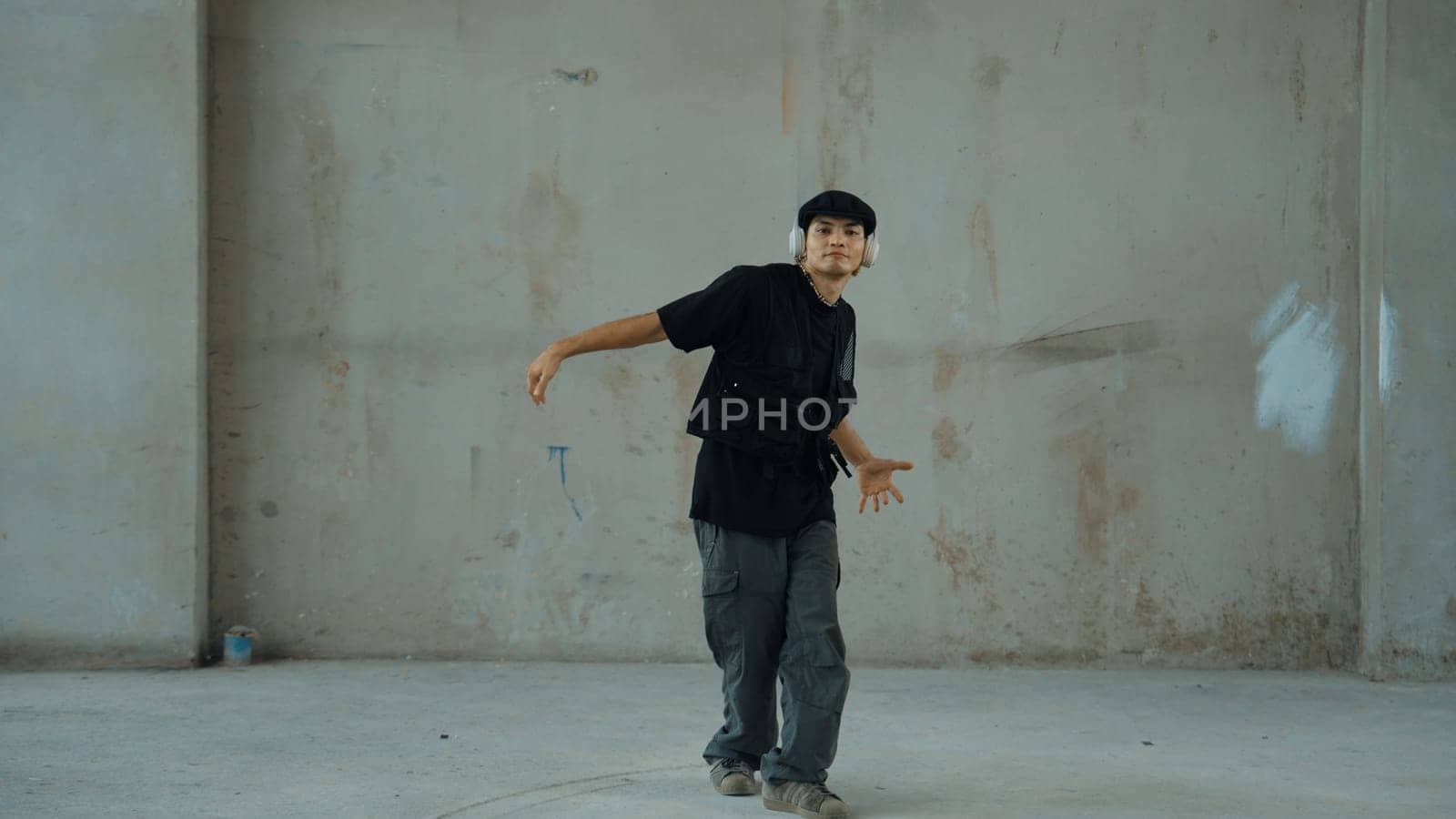 Handsome hipster practicing break dancing while listening music from headphone with cement background. Motion shot of street dancer perform robot dance. Outdoor sport 2024. Modern dance. Endeavor.
