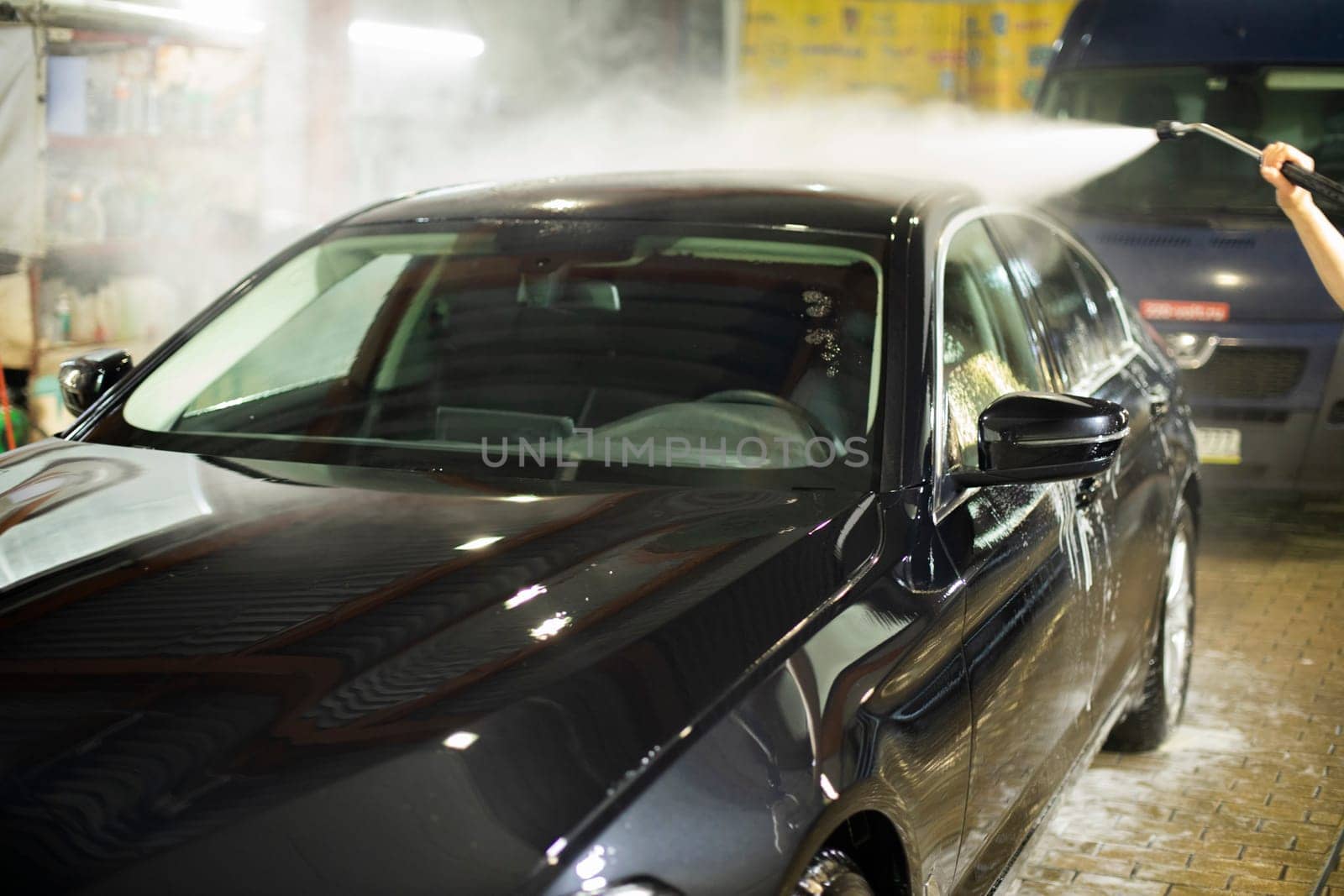 Car wash. Black car in car wash. Hot water jet. Washing off dirt from vehicle.