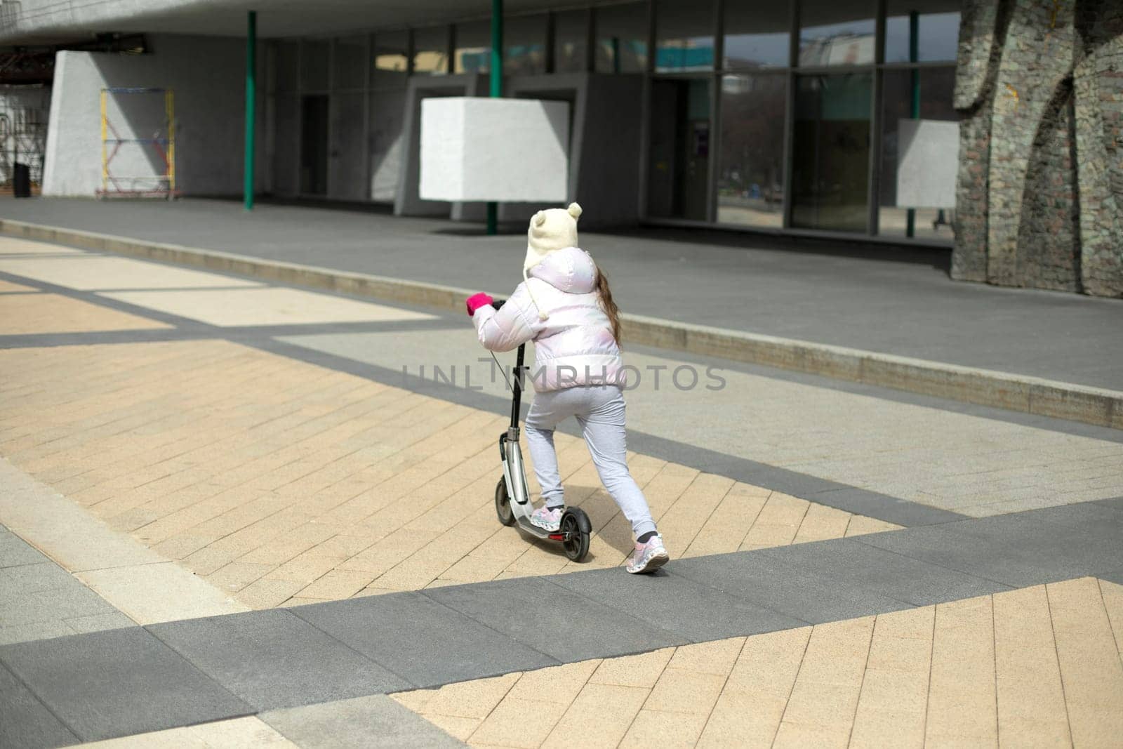 Child on scooter. Girl rides around square. Child travels by mechanical transport. by OlegKopyov