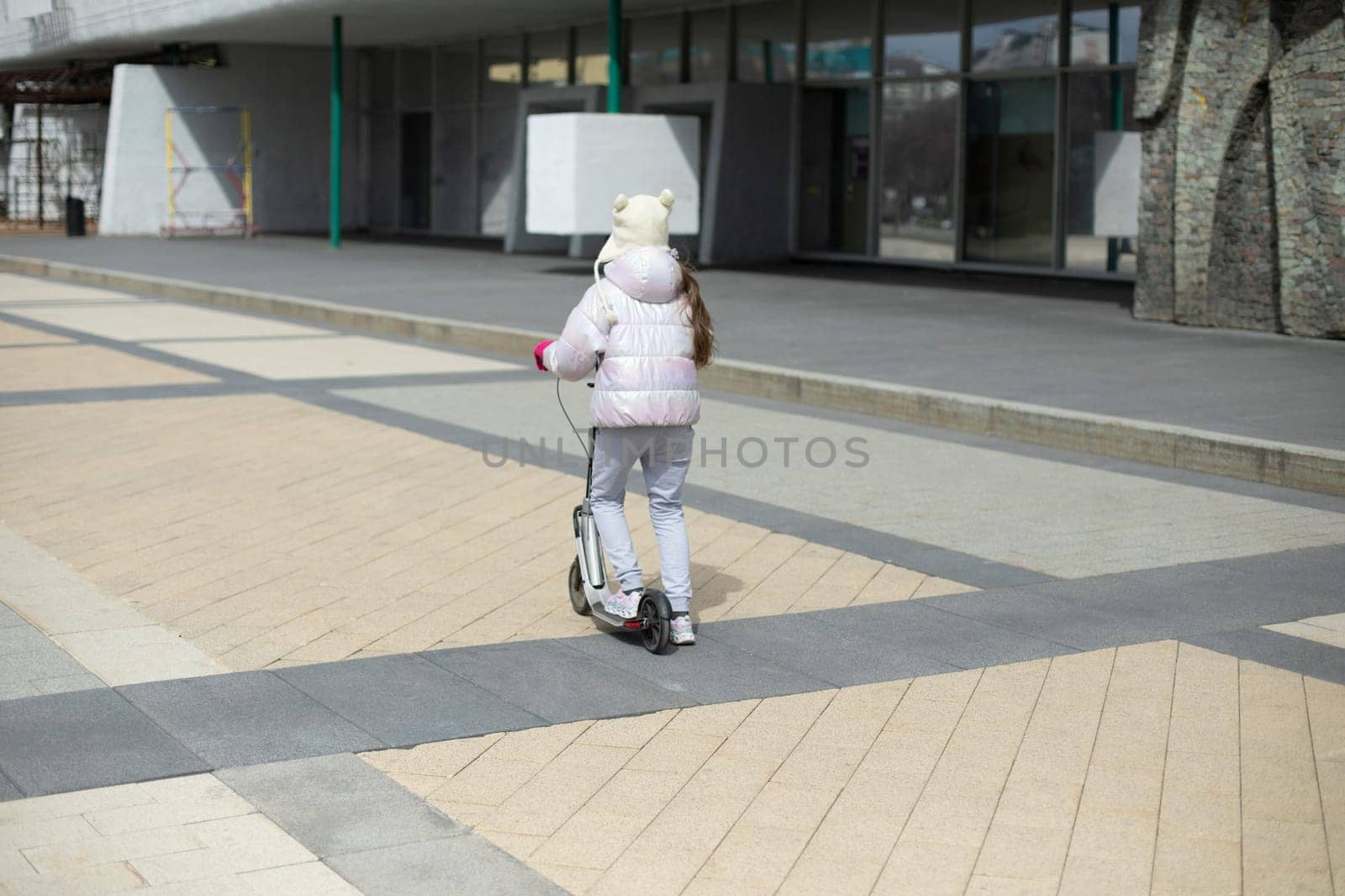 Child on scooter. Girl rides around square. Child travels by mechanical transport. by OlegKopyov