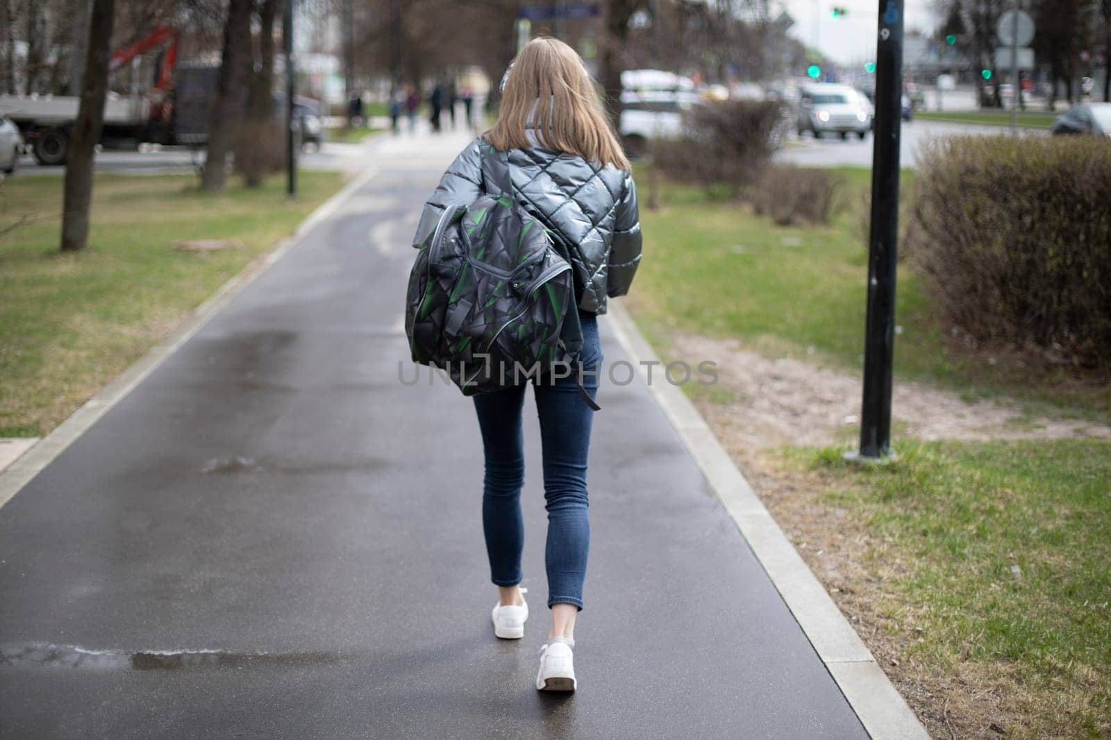 Woman walks through city. Girl in jeans on street. Backpack and jacket. by OlegKopyov