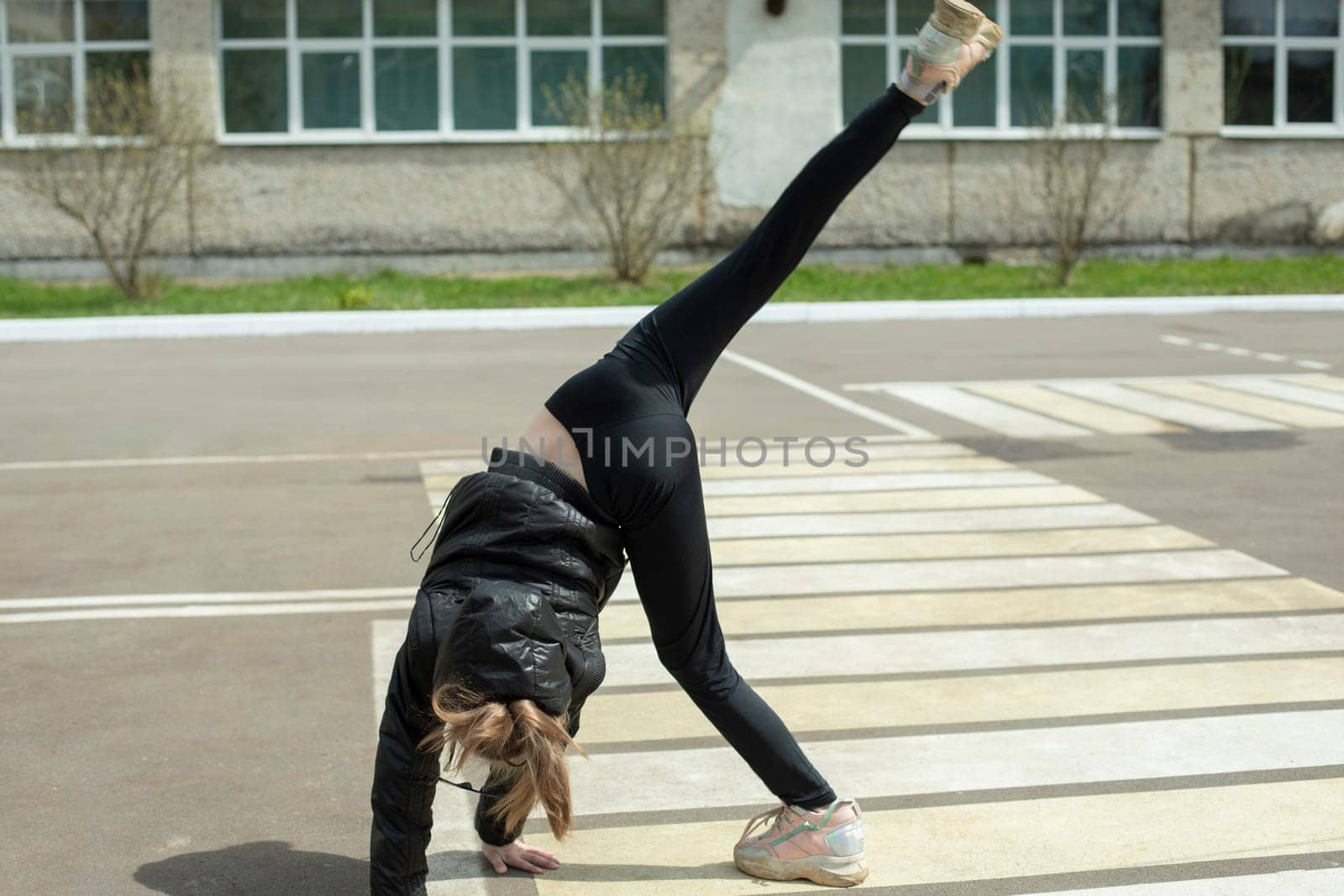 Girl shows acrobatic stunt on street. Child makes wheel on asphalt. Expressive movement. Gymnastics for health. Active lifestyle.