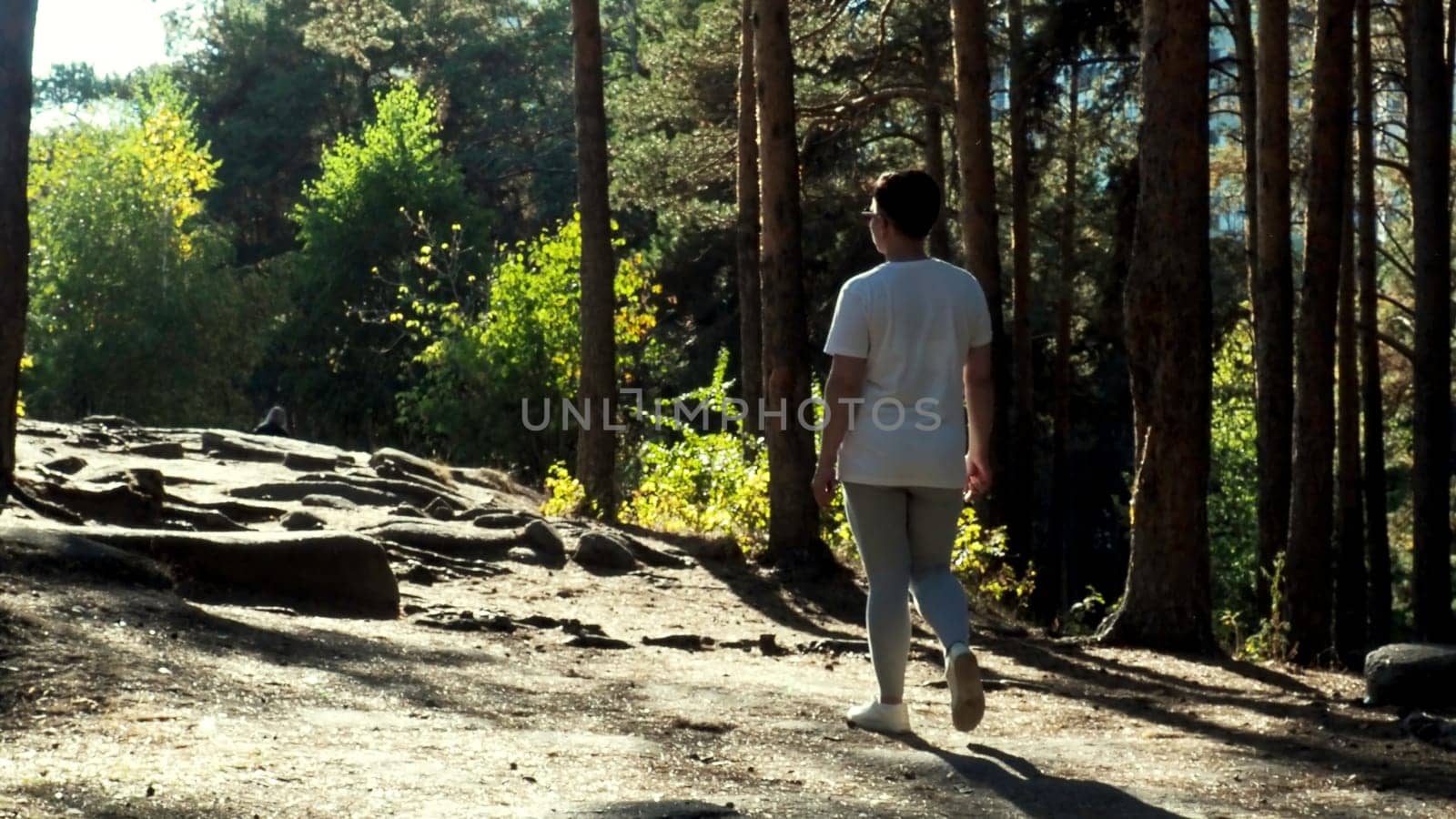 Woman in active wear walking along green forest. Motion. Young athlete woman spending time outdoors, concept of strength and endurance