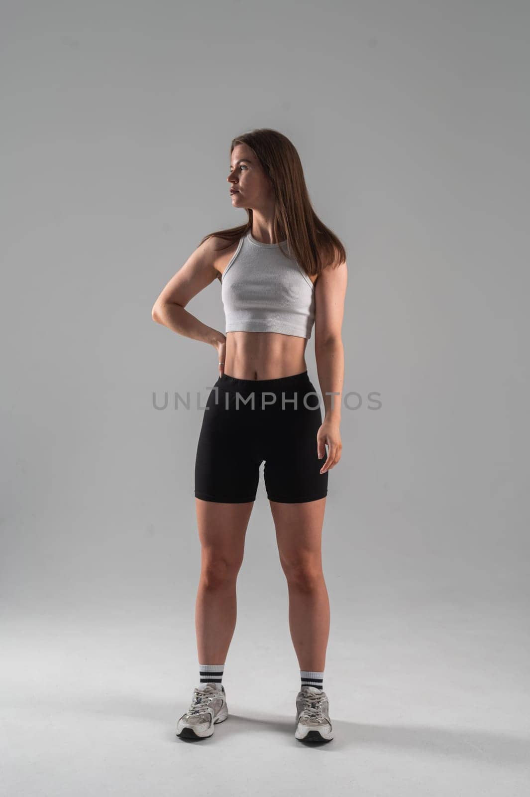 Athletic Caucasian woman in shorts and crop top posing on white background