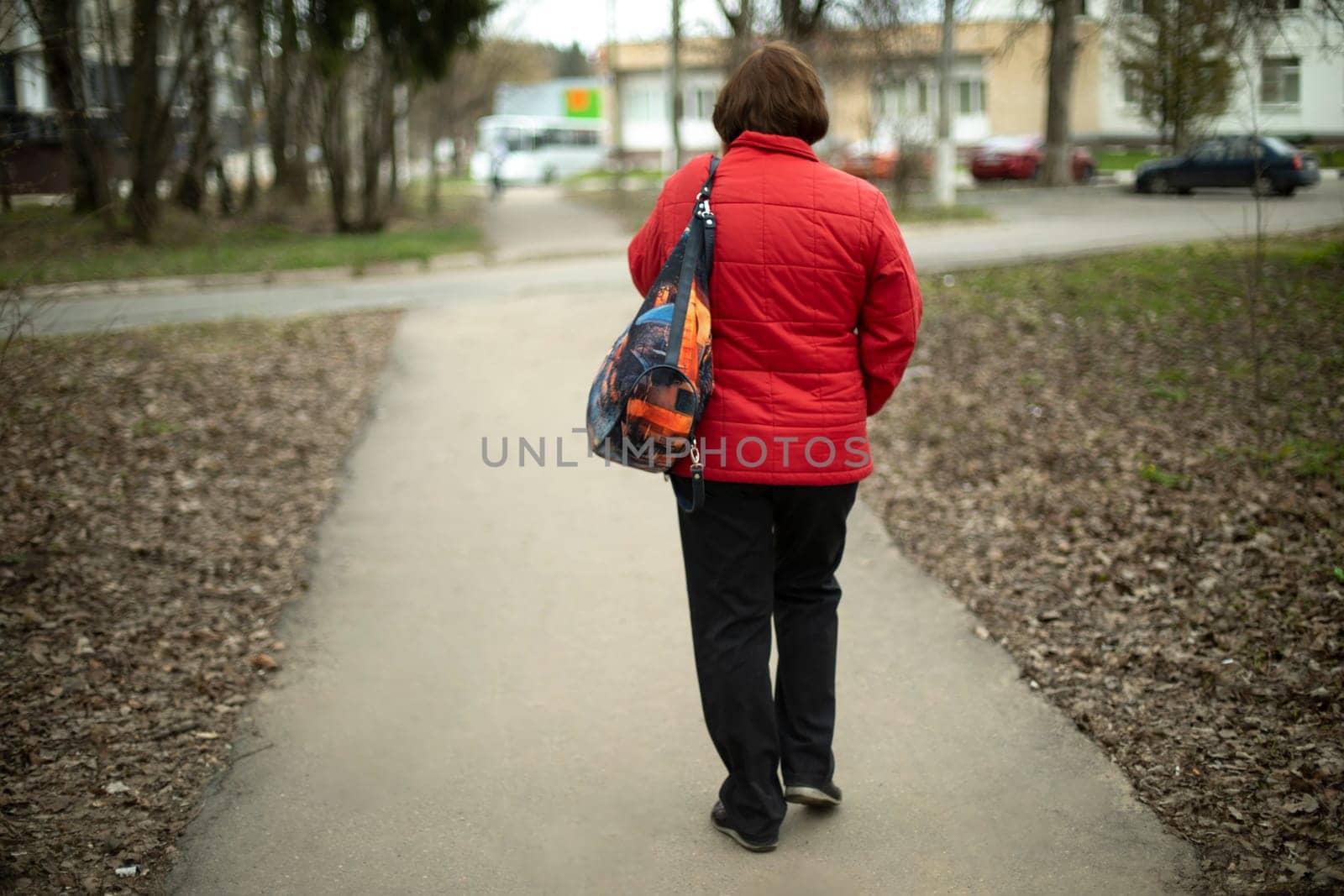Woman in red jacket and black pants. Girl walks through park. Walk in city.