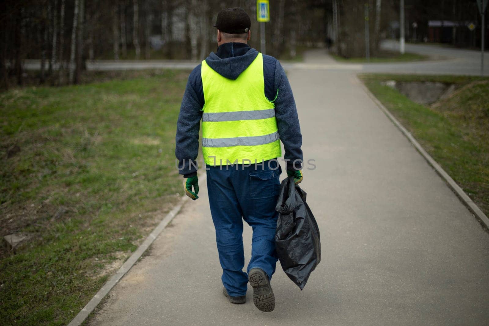 Worker collects garbage. Man carries package. Black bag in his hand. Janitor on road.