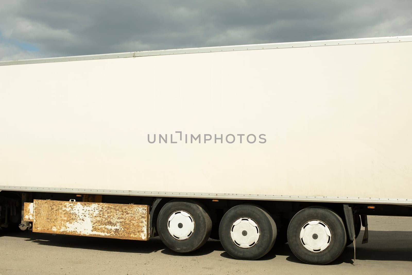 Truck trailer is white. Body of large truck. Transport in parking lot.