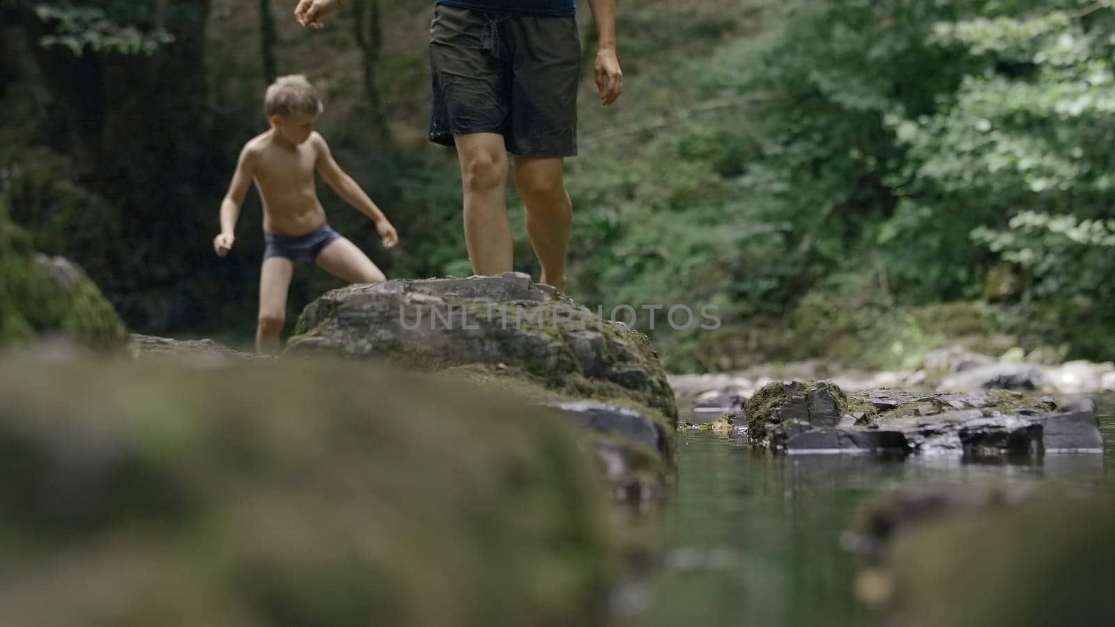 Child and parent walking on moss covered stones near the river. Creative. Boy and his mother or father walking in jungles