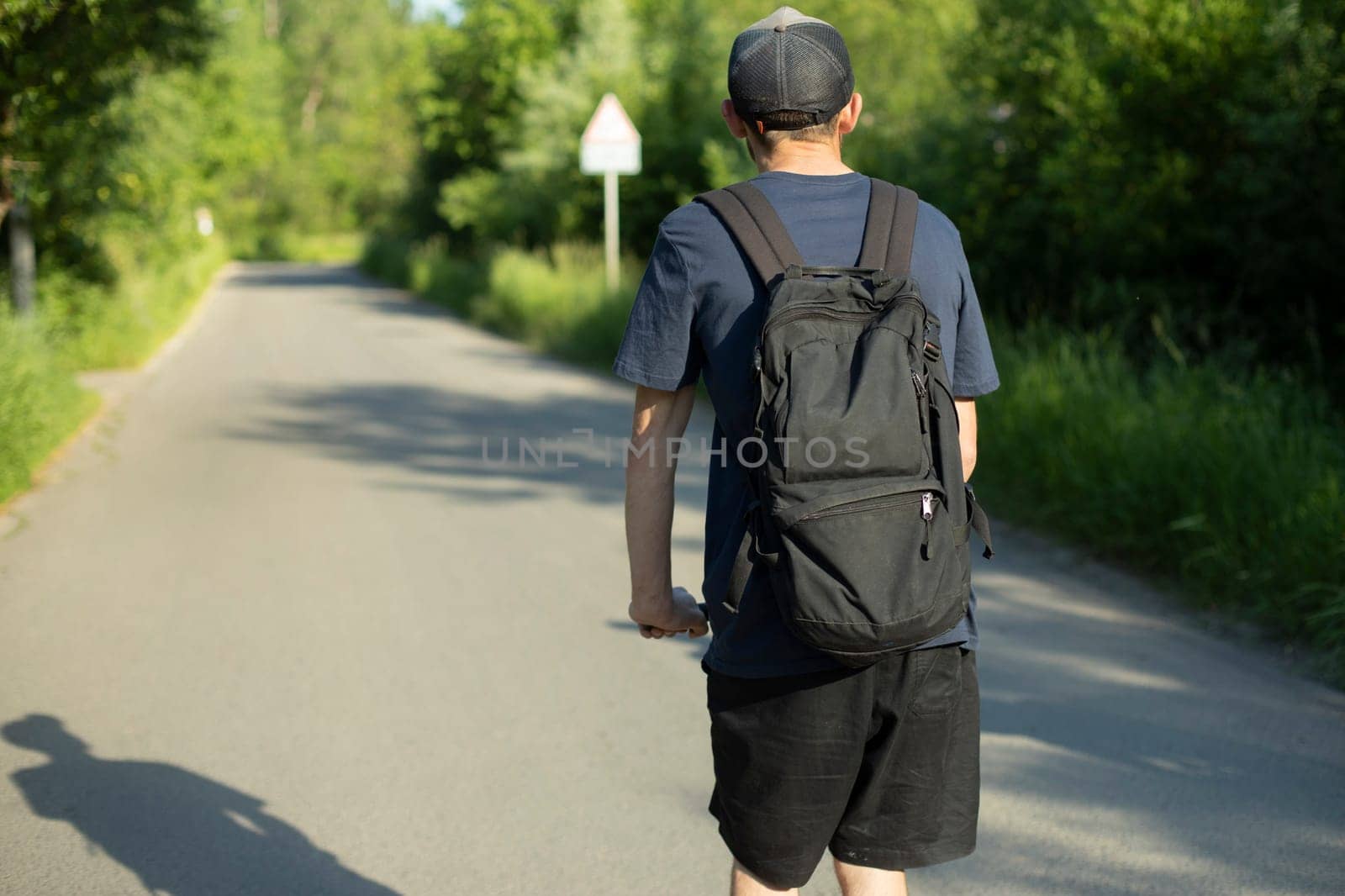 Guy rides scooter down road. Traveling with backpack. Black backpack on back. Traveler on empty road in summer.