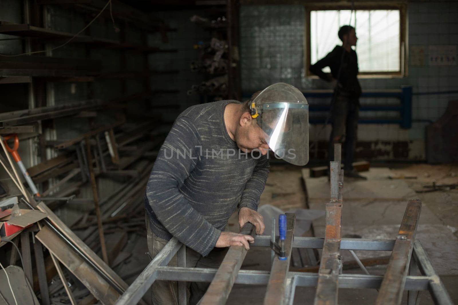 Welder holds metal. People in metal workshop. Work in garage. Worker in protective mask.