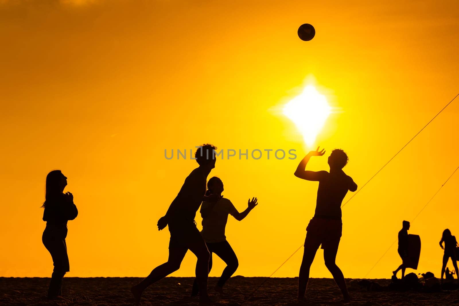 A group of people standing on top of a beach and playing voleiball