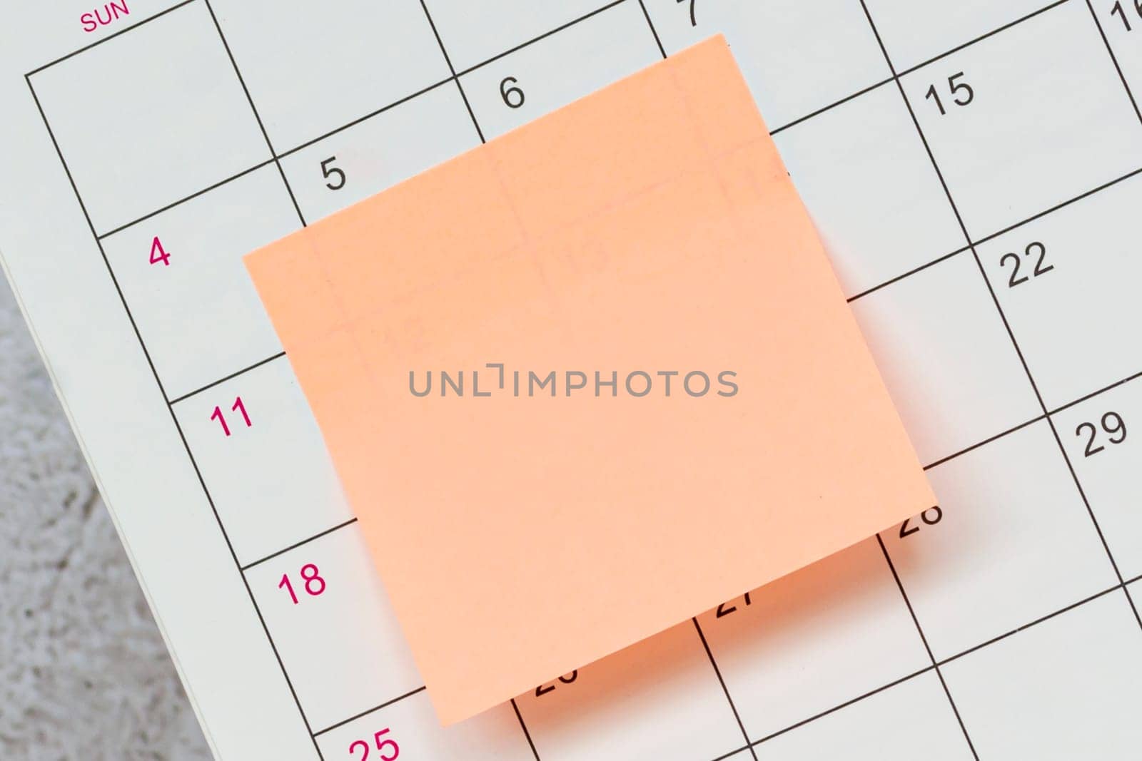 Orange paper sticky note and stuck to a calendar background. Business and reminder concept.