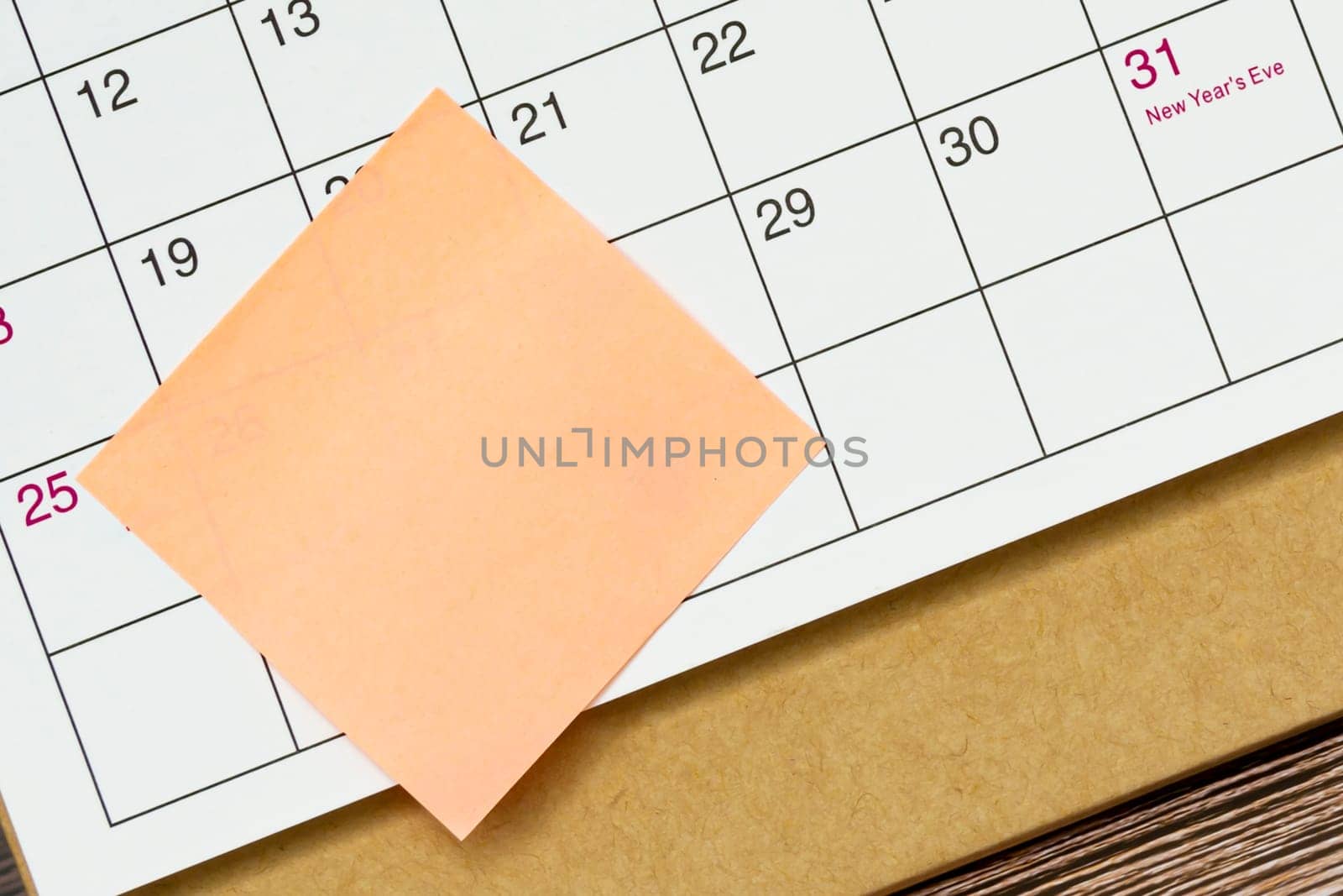 Orange paper sticky note and stuck to a calendar background. Business and reminder concept.