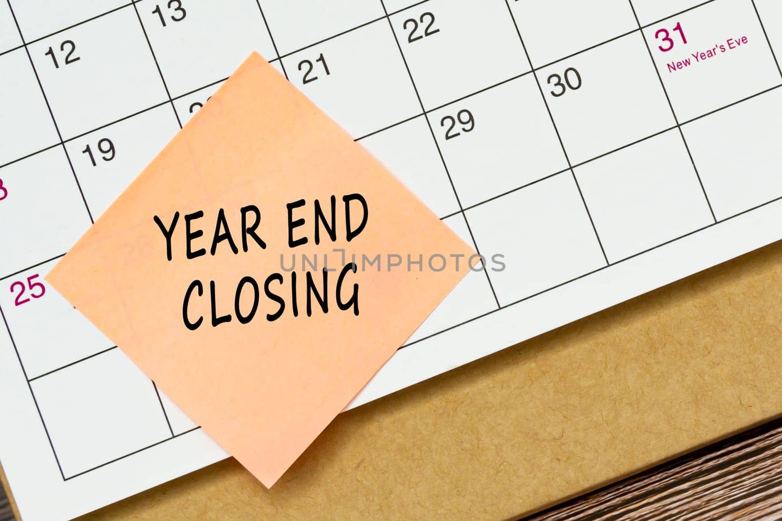 Year end closing text on orange paper sticky note and stuck to a calendar background. Reminder and audit concept.