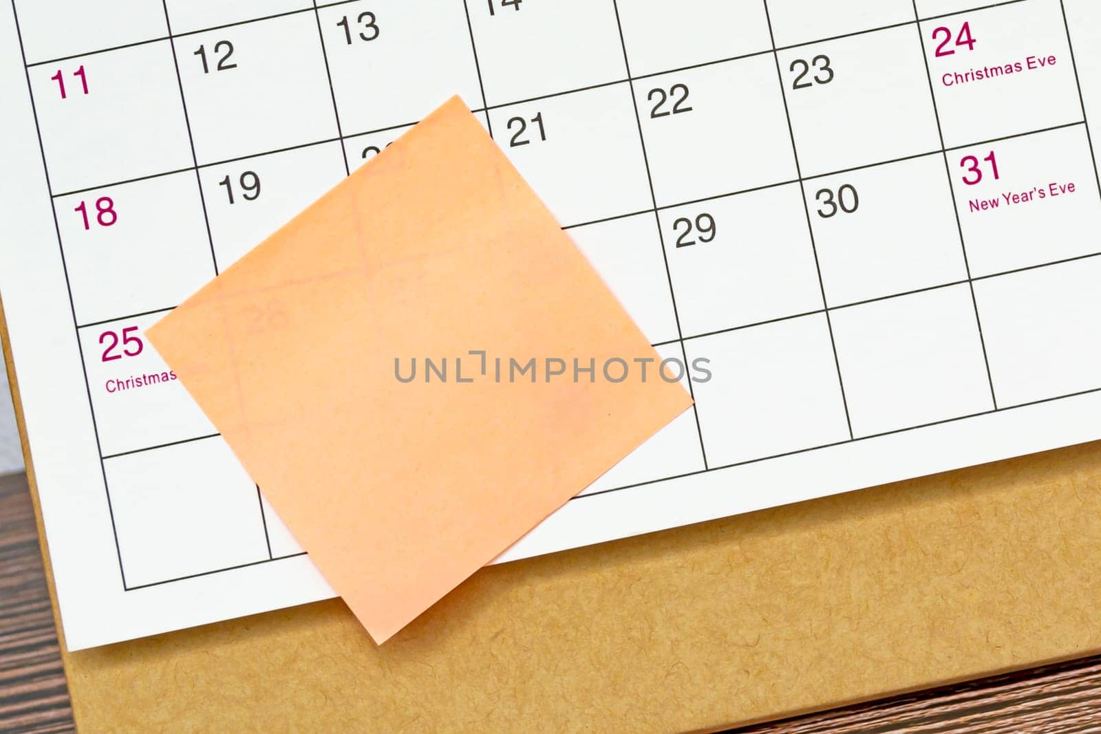 Orange paper sticky note and stuck to a calendar background. Business and reminder concept.